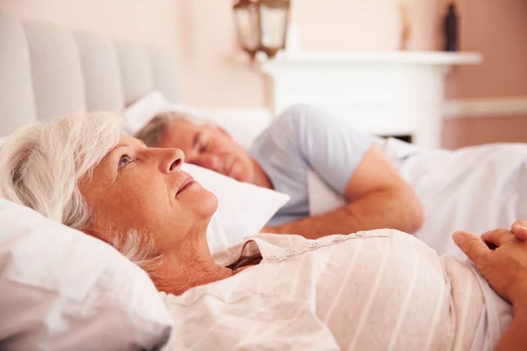 Elderly seniors resting in bed with loved one, peaceful senior home care scene.