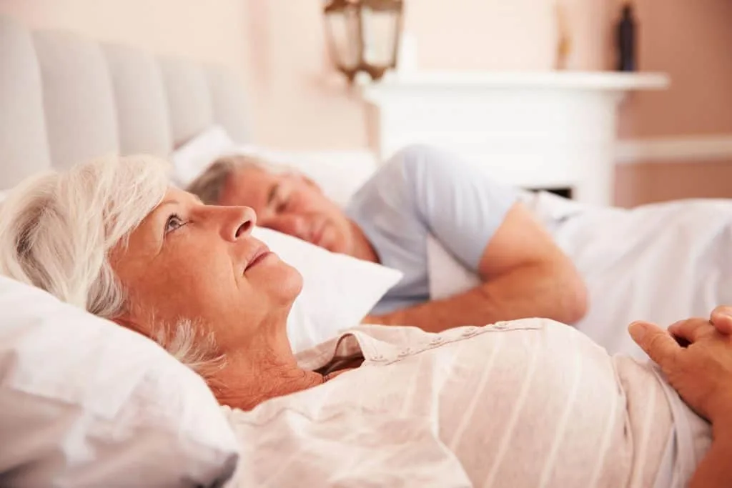 Elderly seniors resting in bed with loved one, peaceful senior home care scene.