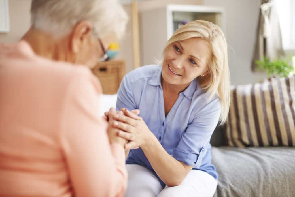 Elderly woman holding hands with caregiver in a warm, home care setting.